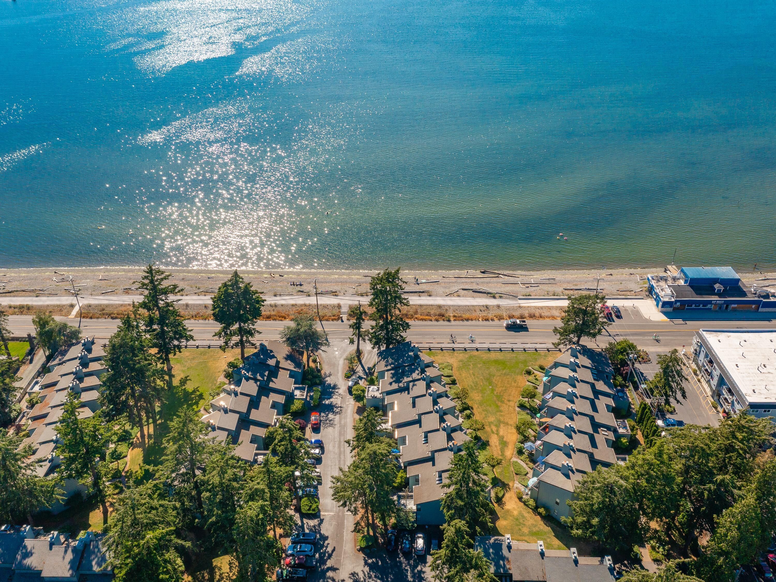 An aerial view of a coastal residential area with houses, a road, and a beach.