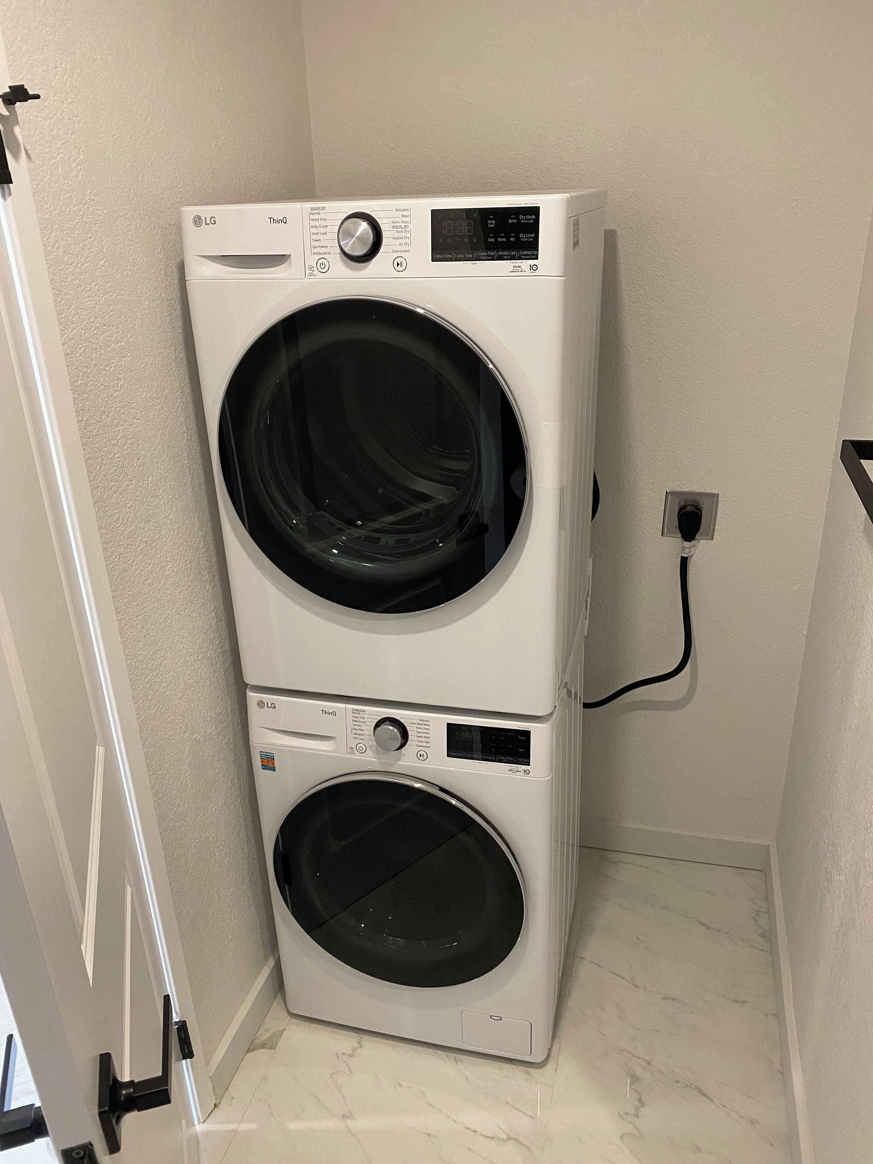 Een gestapelde wasmachine en droger in een wasserij met een marmeren vloer en een witte muur.