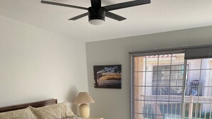 Ein Schlafzimmer mit Bett, Nachttisch, Lampe, einem Gemälde und Blick ins Freie durch ein Fenster.