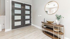 A modern hallway with a dark wooden door, a round mirror, and a console table with a vase and bowl. - Ultimate Lake Norman Getaway - 6BR, Pool, hot tub, Fire Pit, Kayaks, & Boat Dock (Mooresville)