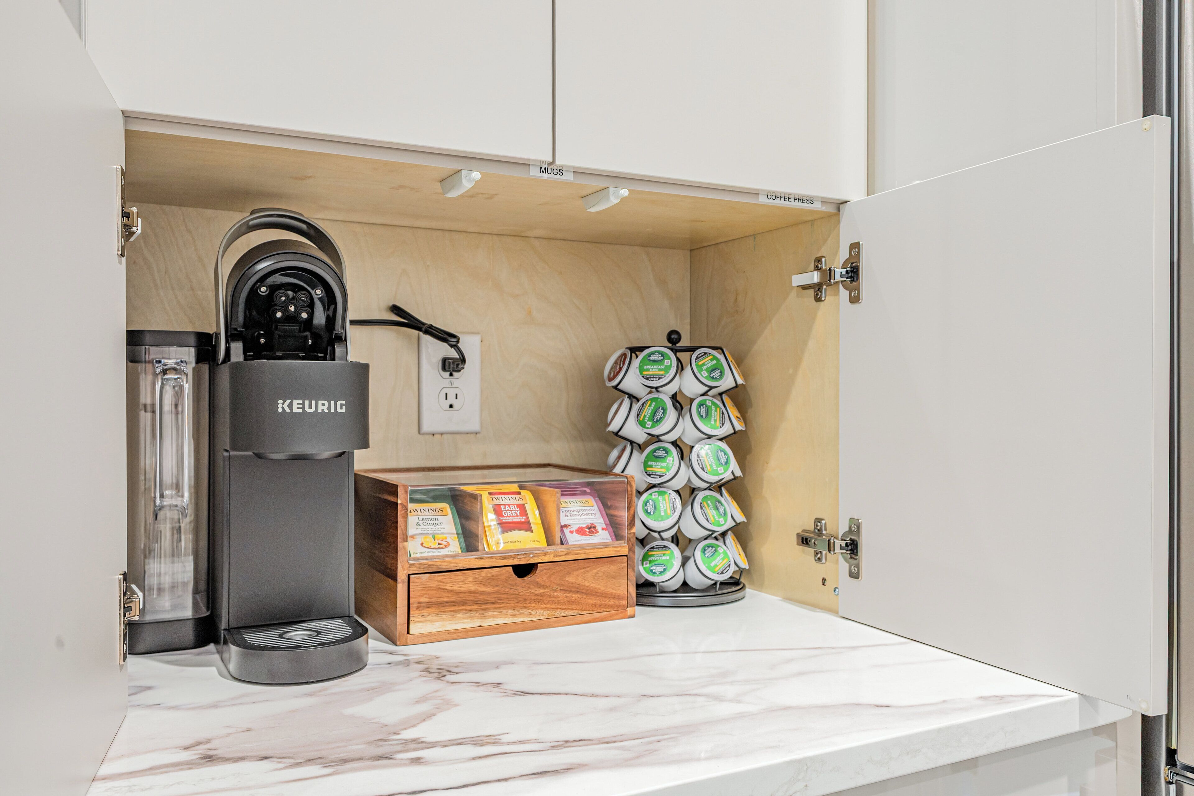 A kitchenette with a Keurig coffee maker, a coffee press, and a box of Twinings coffee pods.