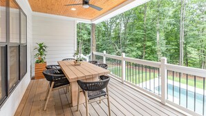 A wooden deck with a table and chairs, a ceiling fan, and a view of a swimming pool and trees. - Ultimate Lake Norman Getaway - 6BR, Pool, hot tub, Fire Pit, Kayaks, & Boat Dock (Mooresville)