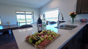 A kitchen with a large island, a dining area with chairs, a view through the windows, and a sink.
