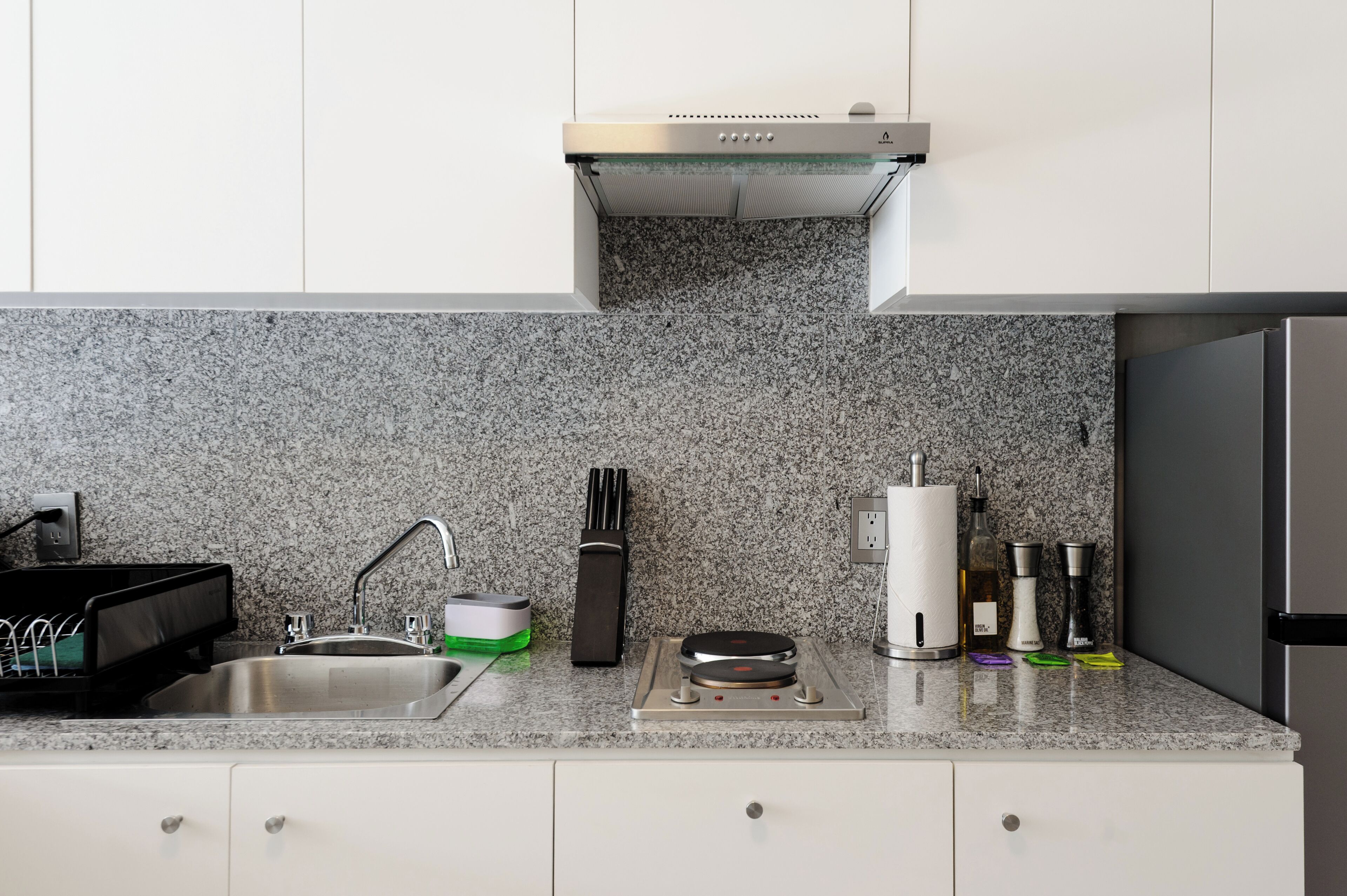 Een keuken met een granieten aanrecht, een roestvrijstalen spoelbak en een inbouw afzuigkap.