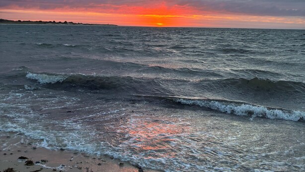 A beach with waves, a sunset, and a cloudy sky.