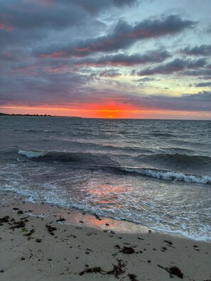 Ein Strand mit Wellen, Sonnenuntergang und bewölktem Himmel.