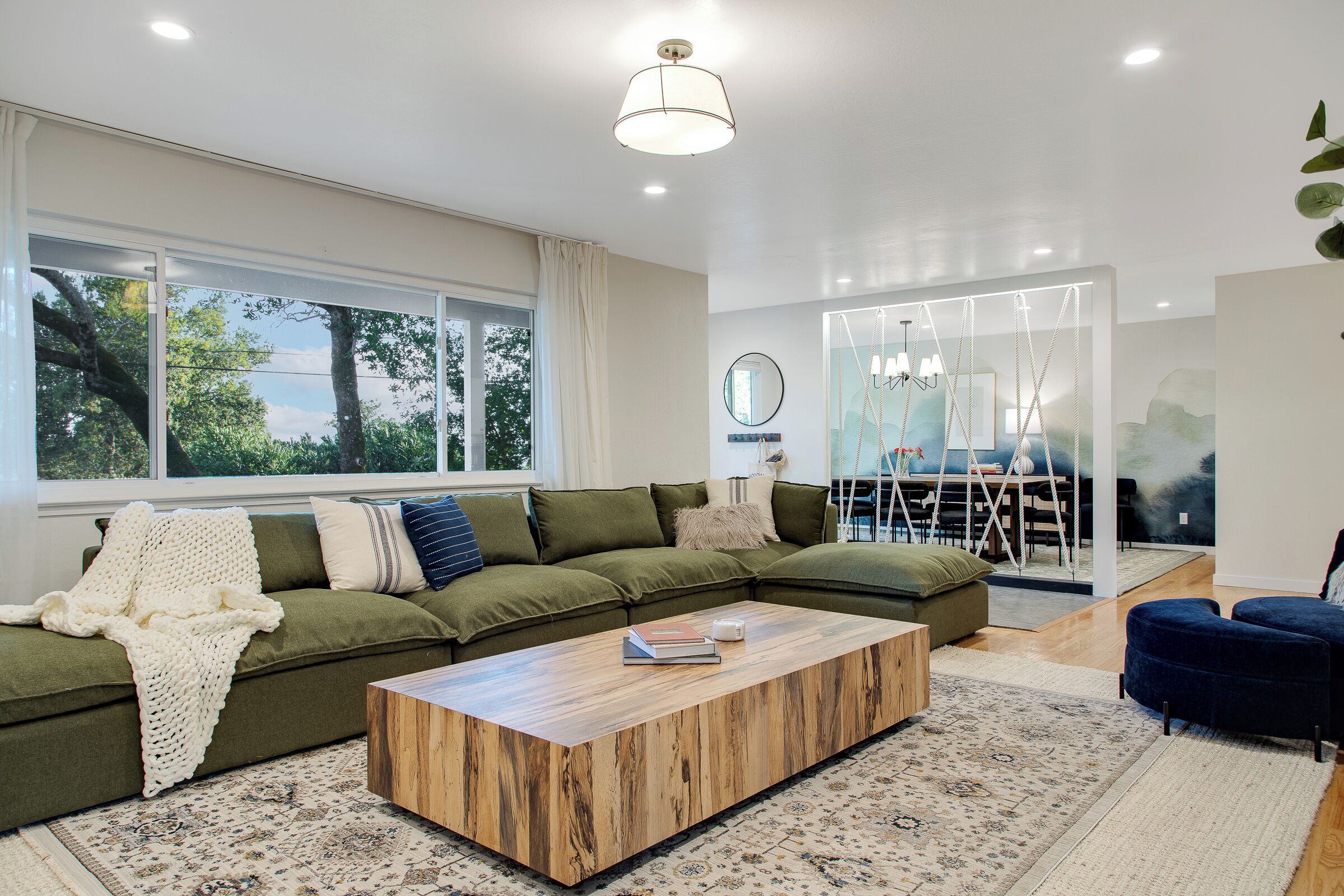 A modern living room with a sectional sofa, a wooden coffee table, and a large window with curtains.