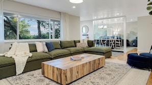A modern living room with a sectional sofa, a wooden coffee table, and a large window with curtains. - Luxury 6-Sleeper: Pool, HotTub, 8 mins to Sonoma Square, and Deluxe Coffee Bar! (Sonoma)