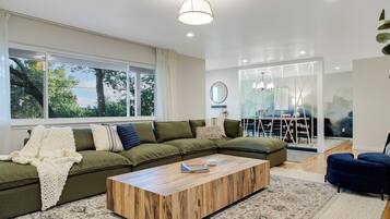 A modern living room with a sectional sofa, a wooden coffee table, and a large window with curtains.