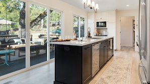 A modern kitchen with a large island, sliding glass doors leading to an outdoor patio, and a built-in microwave. - Luxury 6-Sleeper: Pool, HotTub, 8 mins to Sonoma Square, and Deluxe Coffee Bar! (Sonoma)