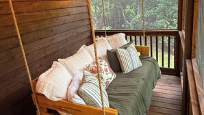 A wooden bed with a hanging swing, string lights, and a view of greenery outside.