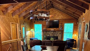 A rustic wooden interior with a dining area, seating, a fireplace, and a TV mounted on the wall.