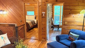 A cozy cabin interior with wooden walls, a bed, a blue sofa, and a dining area.