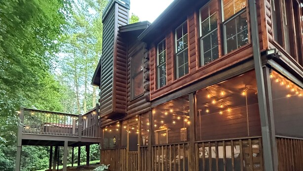 A log cabin with a deck, surrounded by trees.