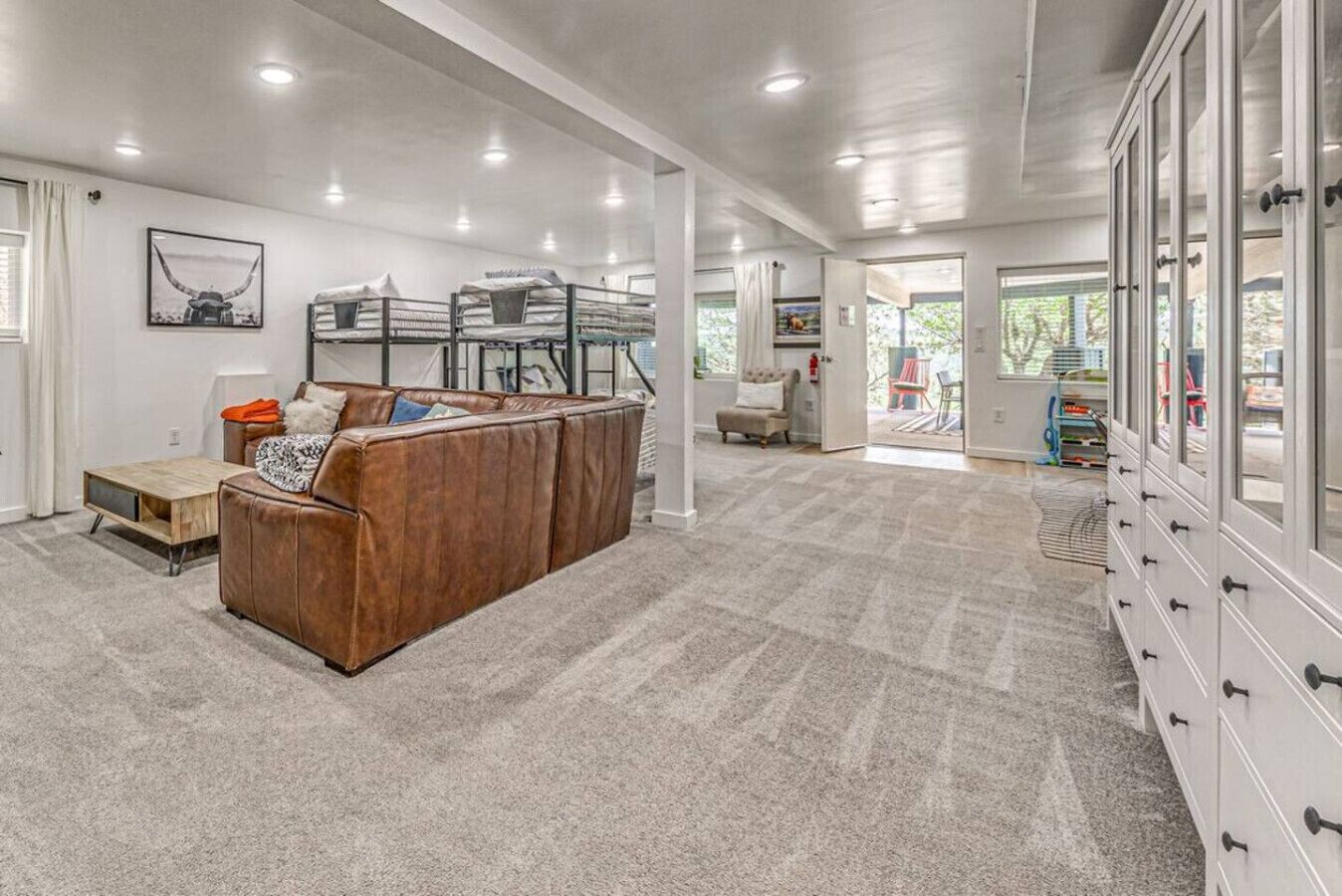 A spacious living area with a brown leather couch, a wooden coffee table, and a large cabinet with drawers.