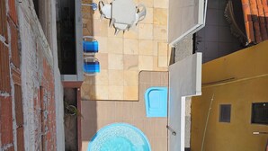 An aerial view of a residential area with a swimming pool, a patio with a table and chairs, and a small garden area.
