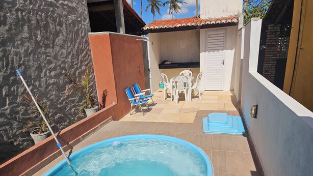 A swimming pool with a blue edge, surrounded by a tiled patio with chairs and a table.