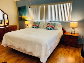 A bedroom with a large bed, two bedside tables, a nightstand, a mirror, and a wall-mounted light fixture.