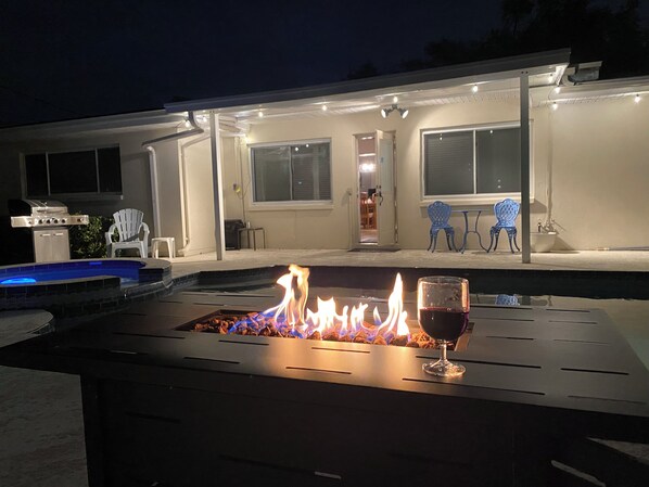 A poolside area with a fire feature and a glass of red wine.