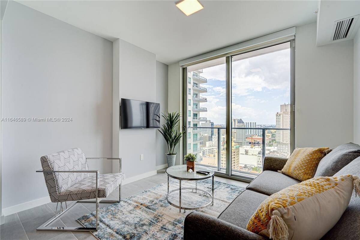 Una sala de estar moderna con un sofá, un sillón y un televisor instalado en la pared.
