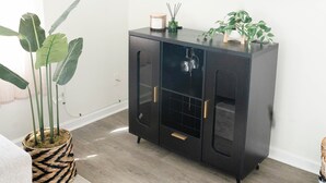 A modern living room with a black cabinet, a large flat-screen TV, and a potted plant. - Cozy Cottage 1.5 mile to  Stadium Ann Arbor (Ann Arbor)