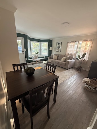 A dining area with a wooden table and chairs, a sofa set, and a window with curtains.