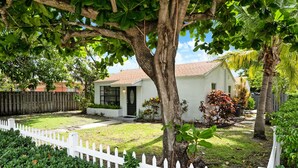 A house with a white picket fence, a well-maintained lawn, and a tree in the foreground.