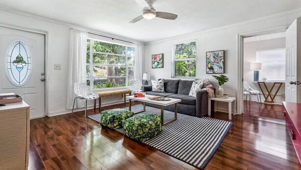 A living room with hardwood flooring, a ceiling fan, a sofa, a coffee table, and a window with curtains.