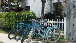 A row of bicycles parked on a sidewalk next to a white fence and a house.