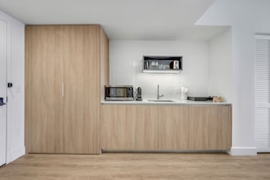 A modern kitchen with wooden cabinets, a microwave, a sink, and a shelf above the counter.