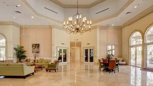 A spacious lobby with a high ceiling, a chandelier, and a polished marble floor. There are seating areas with sofas and a dining table.
