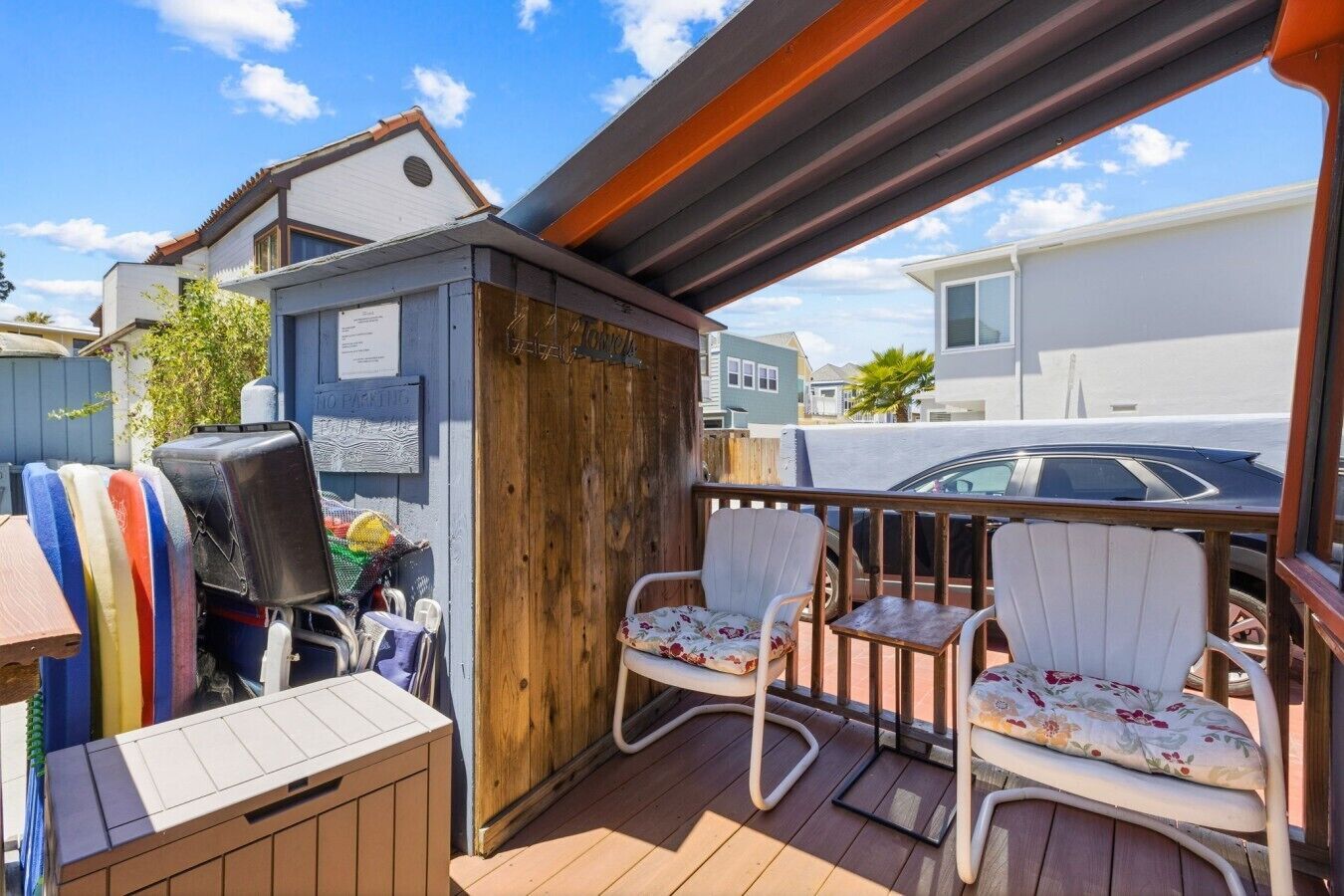 A covered outdoor area with a wooden deck, two white chairs with floral cushions, a barbecue grill, and a small wooden structure.