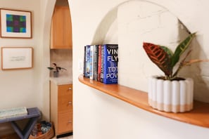 A shelf with books, a plant, and a framed picture on a wall.