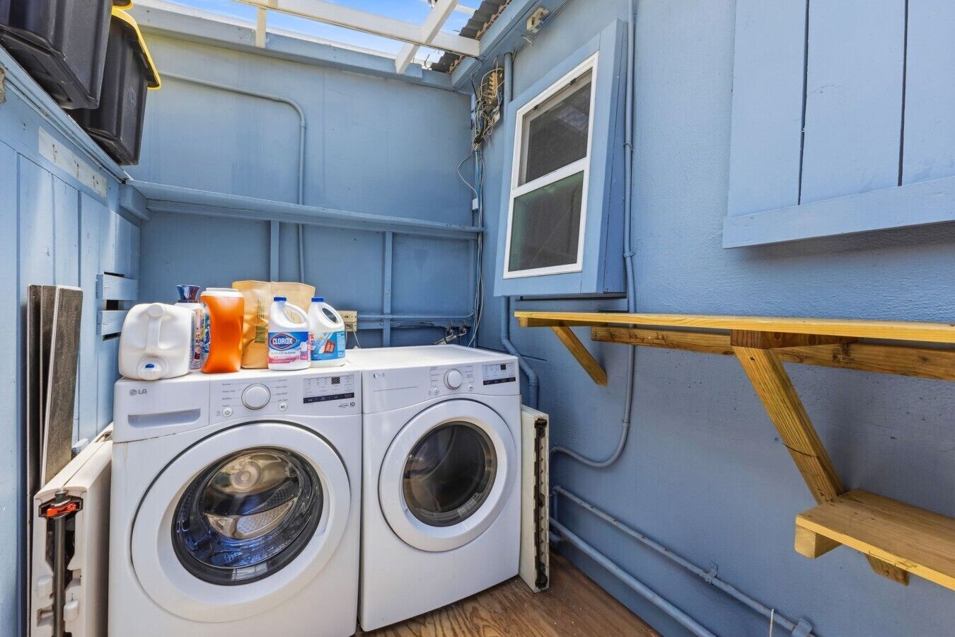 A compact laundry area with two washing machines, a drying rack, and various cleaning supplies.