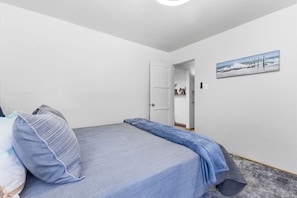 A bedroom with a bed, pillows, a painting, and a door leading to another room.