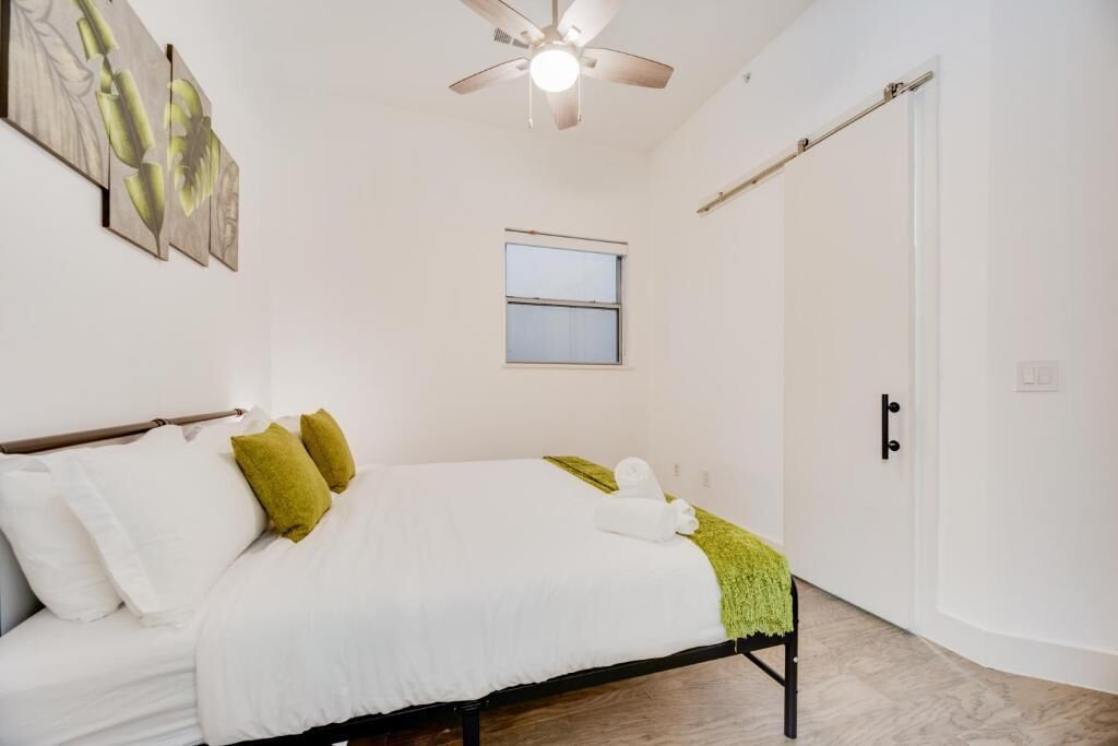 A bedroom with a bed, pillows, a ceiling fan, a window, and a door.