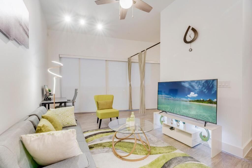 A modern living room with a sofa, a glass coffee table, a television, and a ceiling fan.