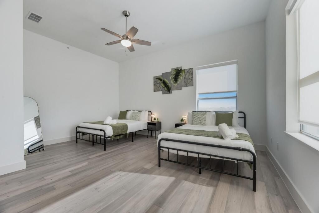 A modern bedroom with two beds, a ceiling fan, and a large window with a view.