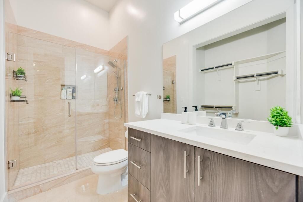 A modern bathroom with a glass-enclosed shower, a white toilet, and a wooden vanity with a mirror.