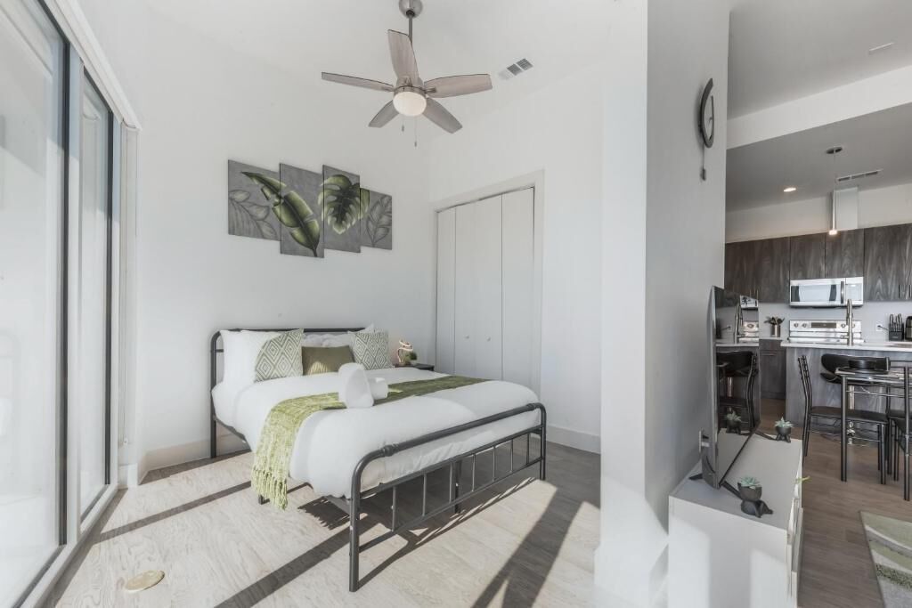 Un dormitorio moderno con una cama, un ventilador de techo y vistas a la cocina contigua.