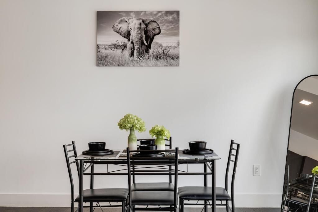 A dining area with a table set for four, featuring black chairs and a black tablecloth. There are two vases with green flowers on the table.