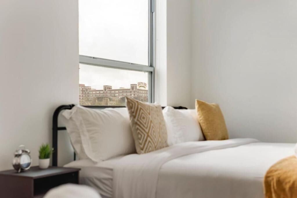Ein Schlafzimmer mit einem Bett, einem Nachttisch mit Pflanze und einem Fenster mit Blick auf Gebäude.