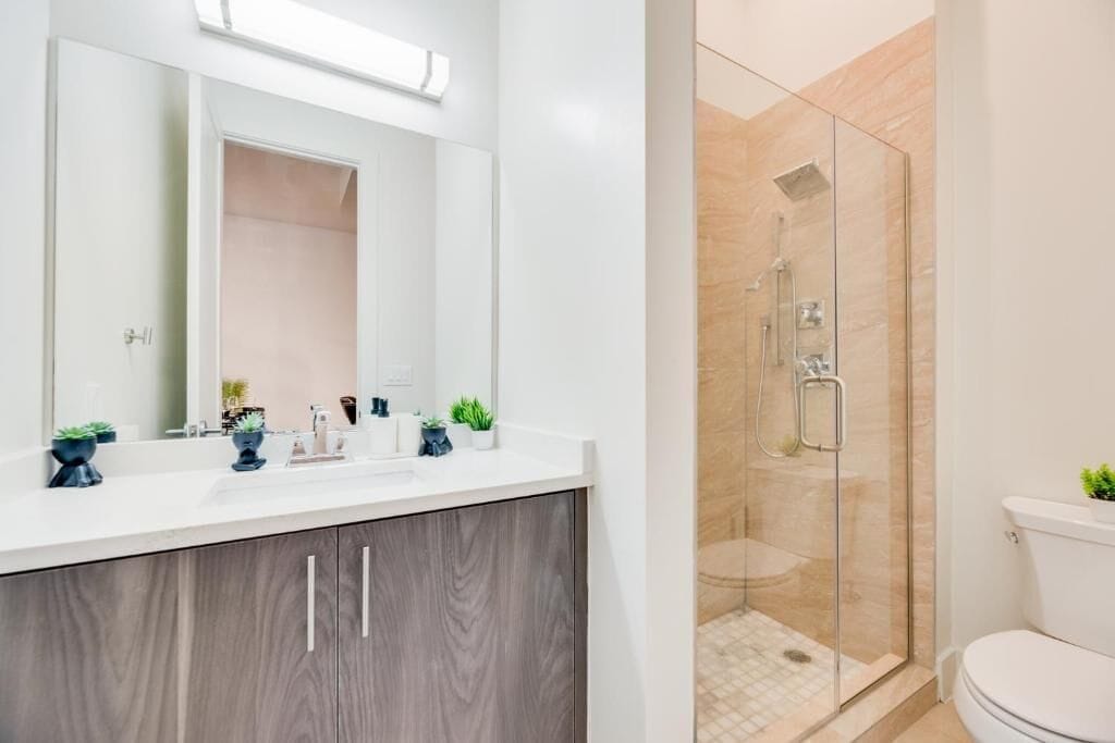 Un baño moderno con tocador blanco, un espejo grande y ducha con mampara de vidrio.