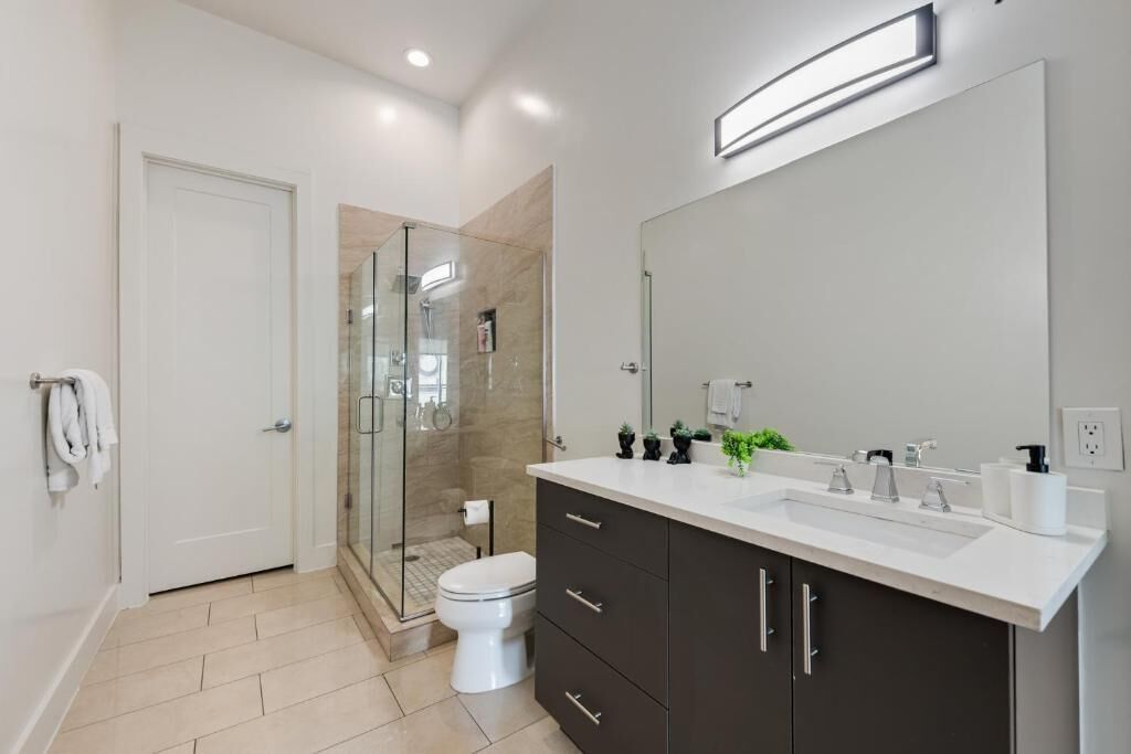 Een moderne badkamer met een douchecabine van glas, een wit toilet en een donkere wastafel met een grote spiegel.