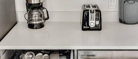 A kitchen with a coffee maker, toaster, and a drawer with kitchen utensils.