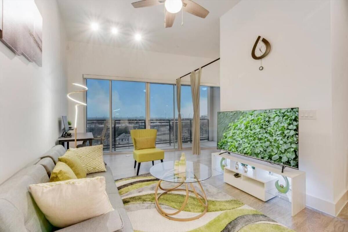 Ein großzügiges Wohnzimmer mit großem Fenster, Deckenventilator, Flachbildfernseher und einer modernen Couch.