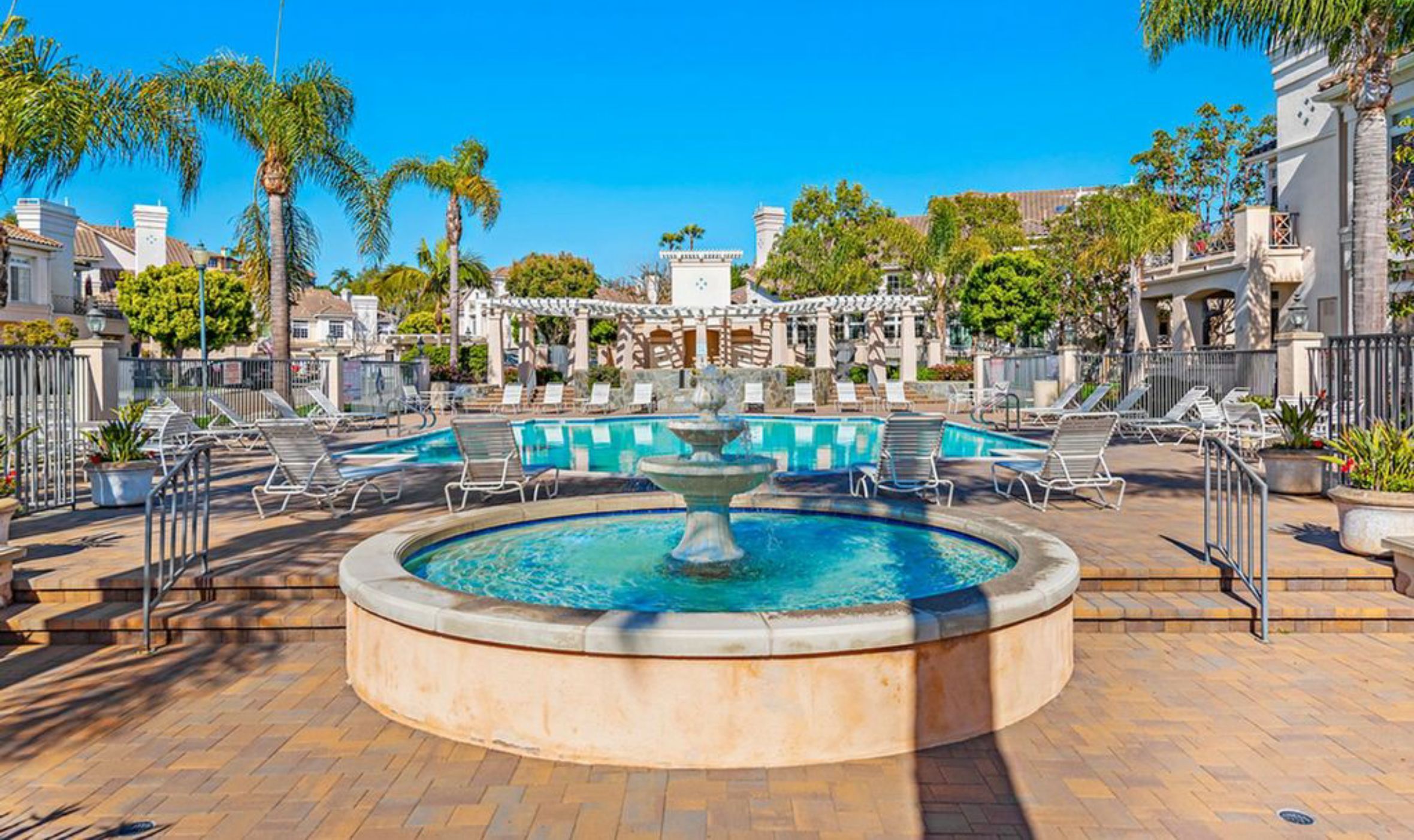 Un espace piscine agrémenté d’une fontaine, de chaises longues et de palmiers.