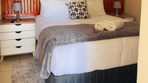 Ein ordentlich bezogenes Bett mit einem gemusterten Bettbezug, zwei Kissen und zusammengerollten Handtüchern an der Kopfteil.