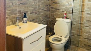 Ein Badezimmer mit Steinwand, einem weißen Waschbecken mit Seifenspender, einer Toilette und einem Fenster über dem Waschbecken.