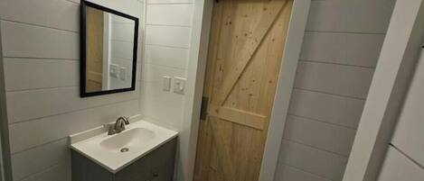 Ein Badezimmer mit einem weißen Waschbecken, einem Spiegel und einer Holztür.